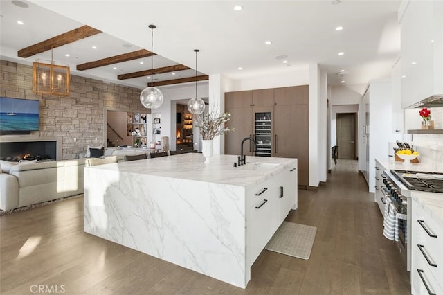 kitchen with white cabinets, decorative light fixtures, high end stainless steel range, a large island, and beam ceiling