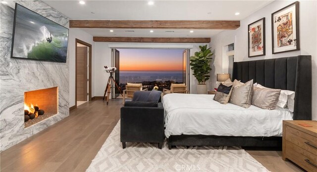 bedroom featuring a premium fireplace, beamed ceiling, and light wood-type flooring