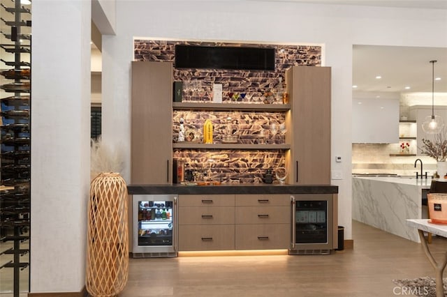 bar with pendant lighting, light wood-type flooring, sink, and beverage cooler