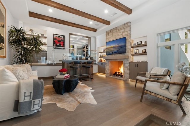 living room featuring beamed ceiling, hardwood / wood-style floors, and a stone fireplace