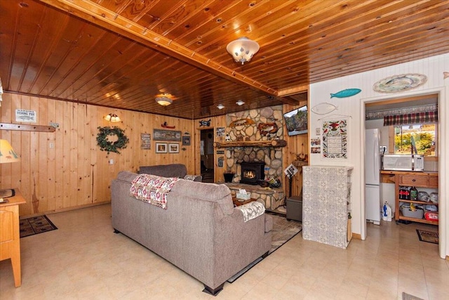 living room with wood ceiling, a stone fireplace, and wooden walls