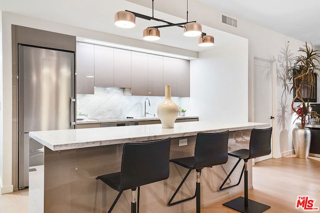 kitchen with a kitchen bar, stainless steel fridge, decorative light fixtures, light wood-type flooring, and tasteful backsplash