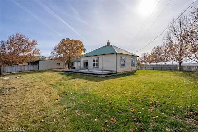 rear view of property with a fenced backyard, metal roof, a lawn, and a wooden deck