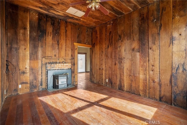 unfurnished living room featuring a ceiling fan, wood ceiling, a wood stove, wood walls, and wood finished floors