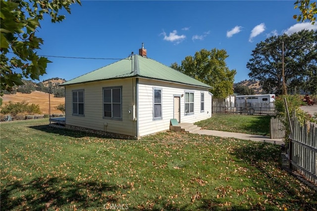 rear view of house featuring a chimney, fence, metal roof, and a lawn