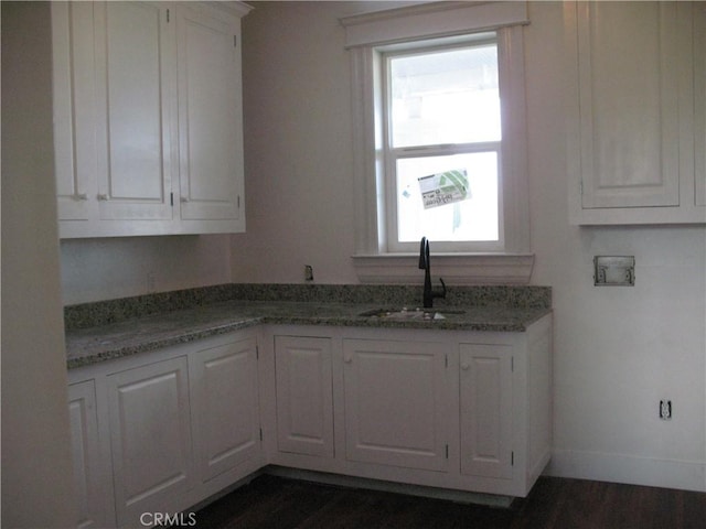 kitchen with stone counters, white cabinetry, and sink