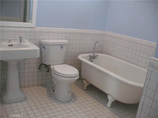 bathroom with tile patterned floors, a tub to relax in, toilet, and tile walls