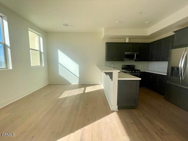kitchen featuring a peninsula, light wood-style flooring, light countertops, appliances with stainless steel finishes, and backsplash