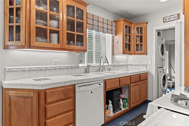 kitchen with tile counters, dishwasher, sink, dark tile patterned floors, and stacked washer / dryer