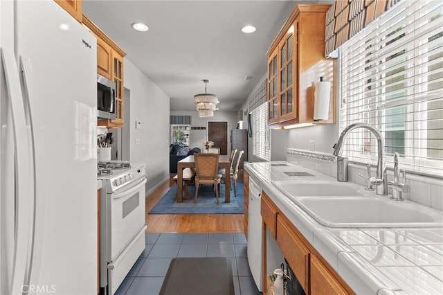 kitchen with sink, dark hardwood / wood-style floors, a notable chandelier, tile countertops, and white appliances