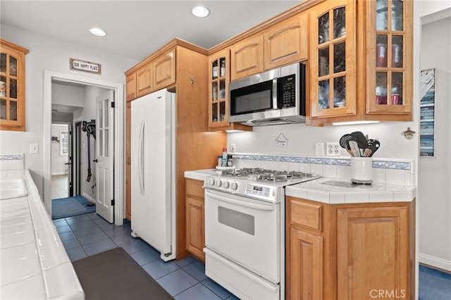 kitchen with light tile patterned floors, white appliances, tile countertops, and sink