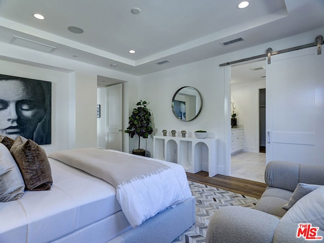 bedroom with ensuite bathroom, a raised ceiling, light wood-type flooring, and a barn door