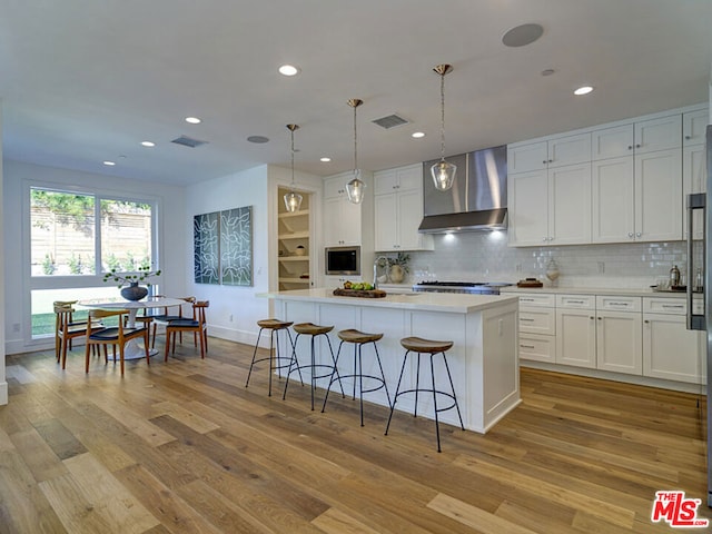 kitchen with wall chimney range hood, white cabinetry, and a kitchen island