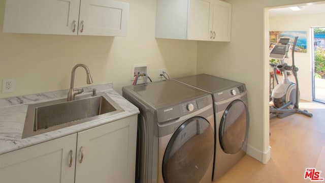 laundry area with cabinets, light wood-type flooring, washing machine and clothes dryer, and sink