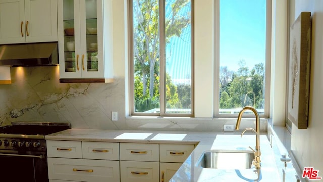 kitchen featuring light stone countertops, stove, sink, exhaust hood, and white cabinetry