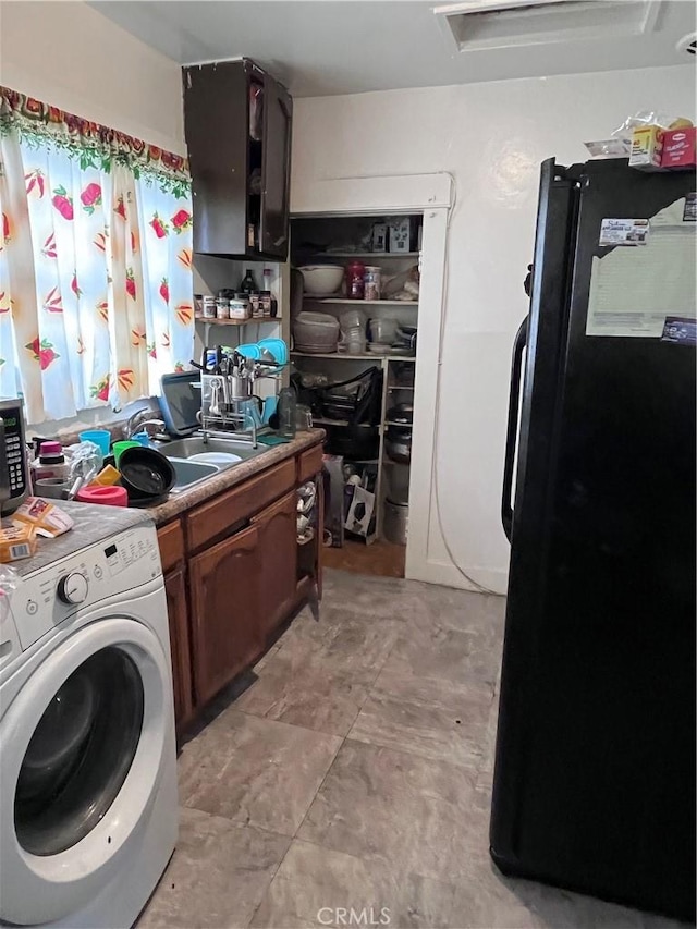 kitchen featuring black fridge, sink, washer / dryer, and light tile floors