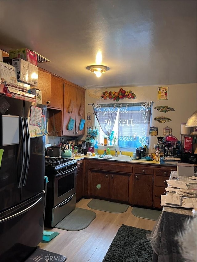 kitchen featuring black refrigerator, sink, gas stove, and light wood-type flooring