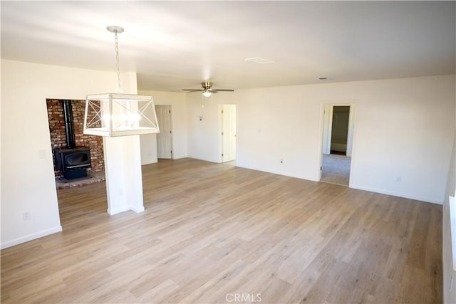 unfurnished living room featuring ceiling fan, light wood-type flooring, and a wood stove