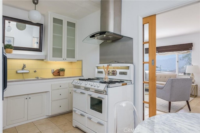 kitchen with wall chimney exhaust hood, white cabinetry, tile countertops, double oven range, and decorative backsplash