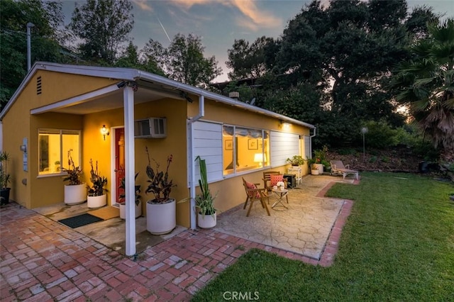 back house at dusk featuring a patio and a lawn