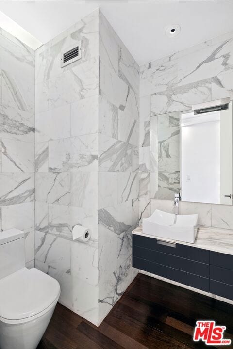 bathroom featuring wood-type flooring, vanity, toilet, and tile walls