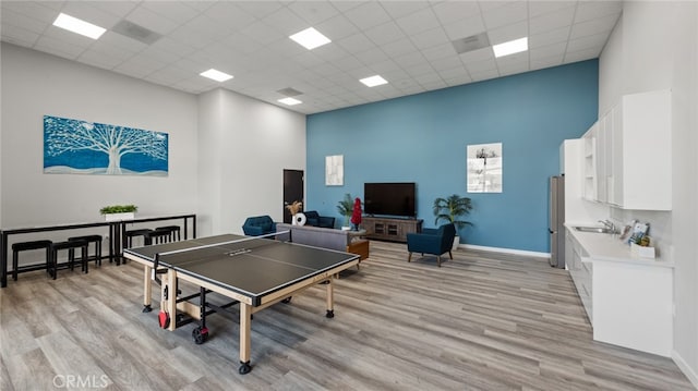 game room with a paneled ceiling, a high ceiling, and light wood-type flooring