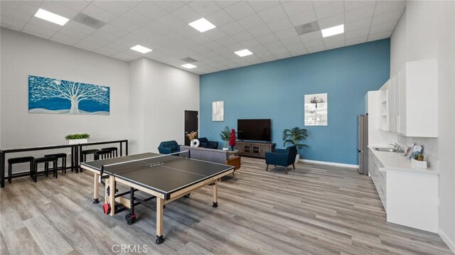 playroom with light hardwood / wood-style flooring, a paneled ceiling, and a towering ceiling