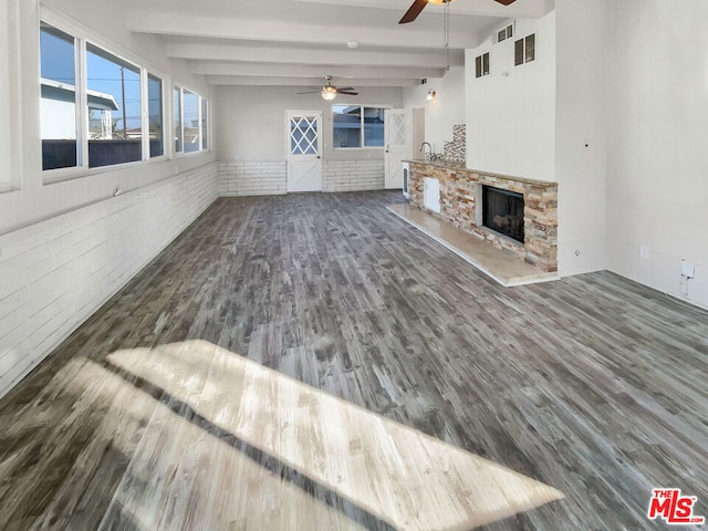 unfurnished living room with a stone fireplace, ceiling fan, beamed ceiling, dark hardwood / wood-style flooring, and brick wall