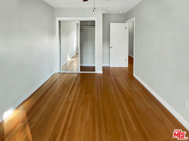 unfurnished bedroom with ceiling fan, a closet, and hardwood / wood-style flooring