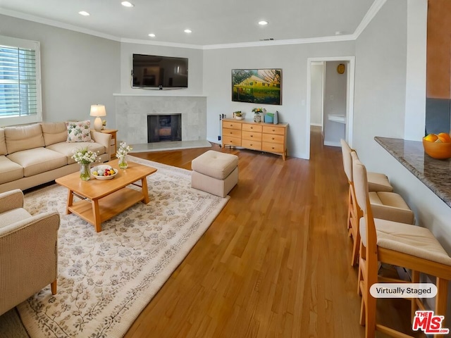 living room featuring a tiled fireplace, crown molding, and light hardwood / wood-style flooring