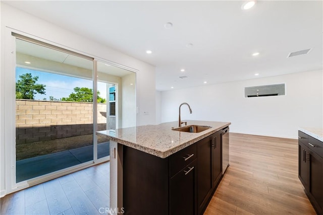 kitchen with dishwasher, a center island with sink, sink, light wood-type flooring, and dark brown cabinets