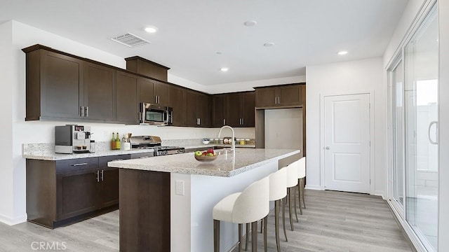 kitchen featuring dark brown cabinets, stainless steel appliances, a kitchen island with sink, sink, and light hardwood / wood-style flooring