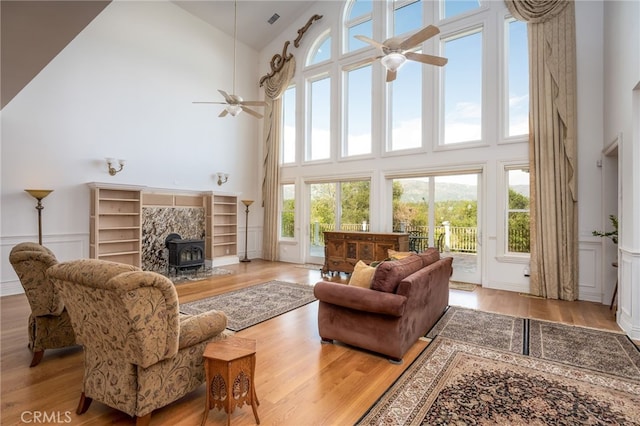 living room with ceiling fan, light hardwood / wood-style floors, a wood stove, and a high ceiling