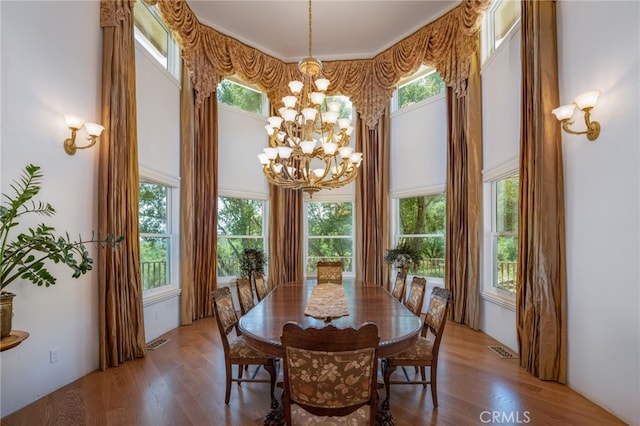 dining space with a towering ceiling, a wealth of natural light, a chandelier, and hardwood / wood-style floors