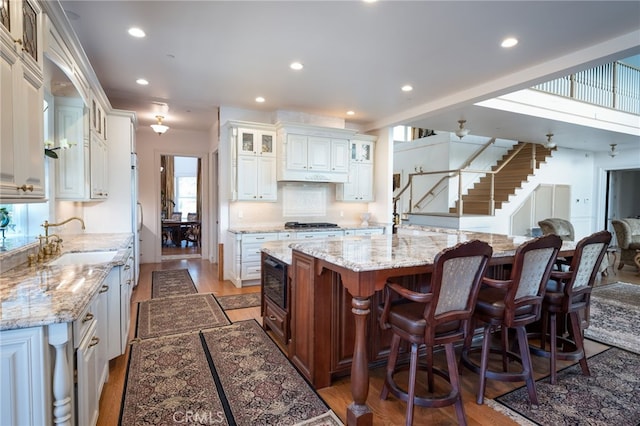 kitchen featuring a breakfast bar area, a spacious island, white cabinets, light stone counters, and sink