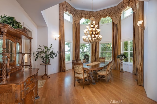 dining area with light hardwood / wood-style floors, a high ceiling, and an inviting chandelier