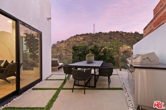 balcony at dusk with a patio area, a mountain view, area for grilling, and grilling area