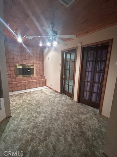 unfurnished living room with ceiling fan, a tiled fireplace, and carpet flooring