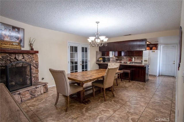 dining area featuring a stone fireplace, a textured ceiling, an inviting chandelier, and french doors