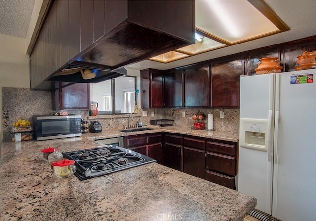 kitchen featuring stainless steel appliances, light stone countertops, dark brown cabinets, and sink