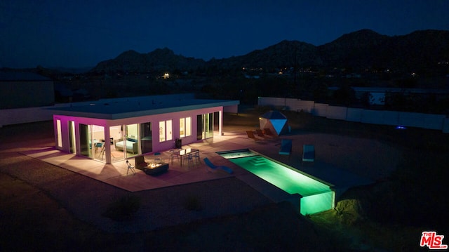 pool at night with a mountain view, a patio area, and an in ground hot tub