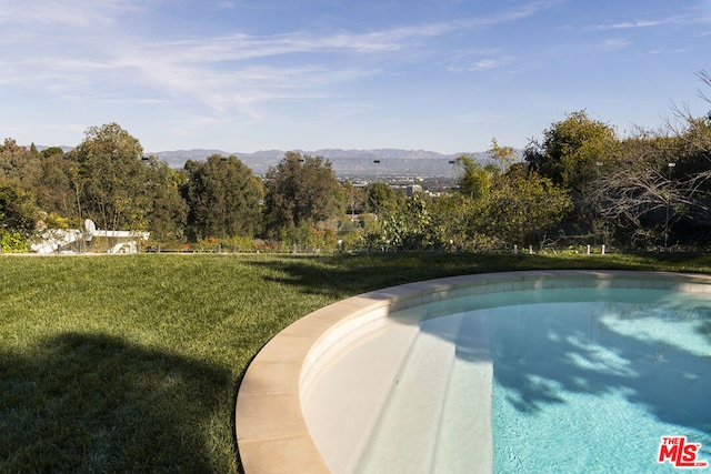 view of swimming pool with a mountain view and a lawn