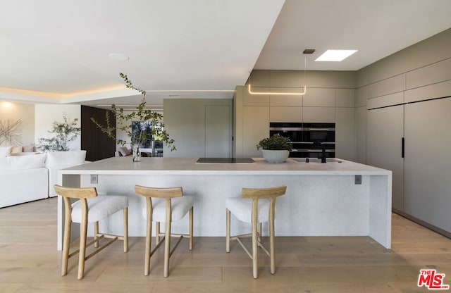 kitchen with a large island, sink, stainless steel oven, and light wood-type flooring