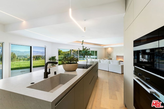 kitchen featuring a spacious island, light hardwood / wood-style flooring, sink, decorative light fixtures, and wall oven