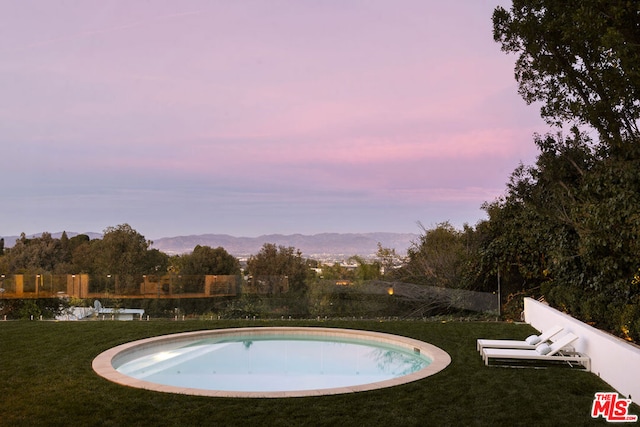 pool at dusk with a mountain view and a lawn