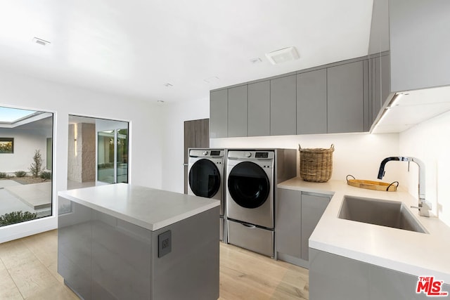 clothes washing area featuring cabinets, light hardwood / wood-style flooring, sink, and washing machine and clothes dryer