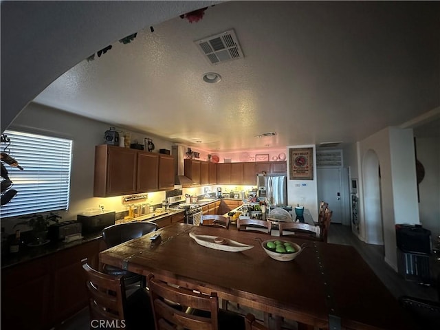 kitchen with a textured ceiling, wall chimney range hood, and appliances with stainless steel finishes