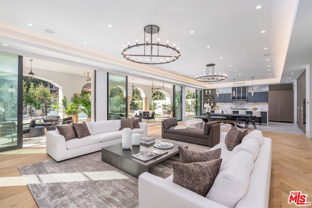 living room with a notable chandelier, light parquet flooring, and a raised ceiling