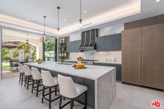 kitchen featuring a large island, wall chimney exhaust hood, a tray ceiling, and pendant lighting