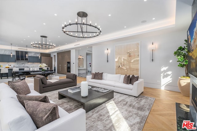 living room featuring a chandelier, light parquet flooring, and a raised ceiling